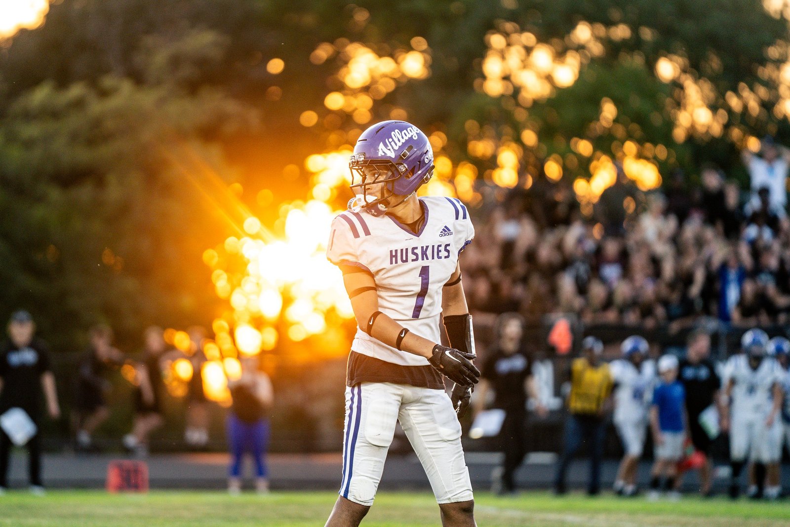 Football player in white with the low sun bursting through trees behind him